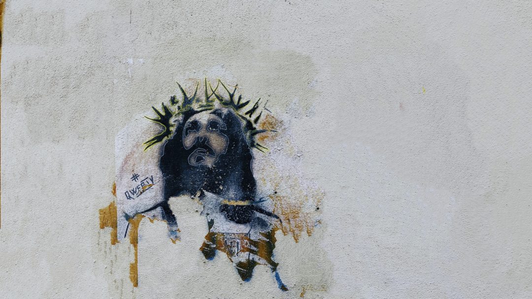 Graffiti art of Jesus with a crown of black thorns against a backdrop of light grey stone.