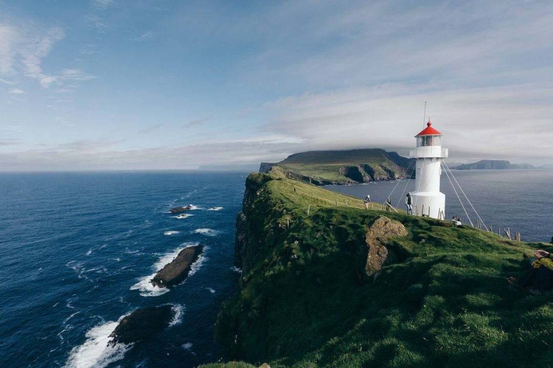 An image of a lighthouse on a cliff near the ocean on a sunny day.
