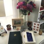 Flowers, painting, journal, books, and altar on white writing desk.